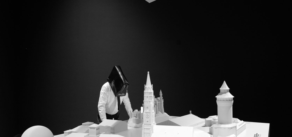 Mann mit Aktentasche am Kopf beugt über Stadtmodell